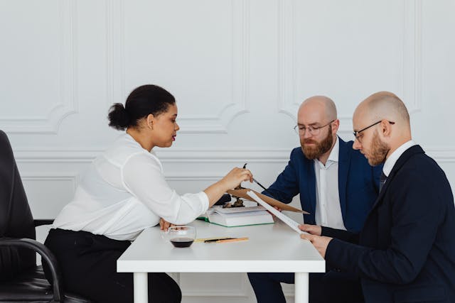 Insurance adjusters and a policyholder reviewing claim documents during a post-disaster settlement meeting in a formal office setting.