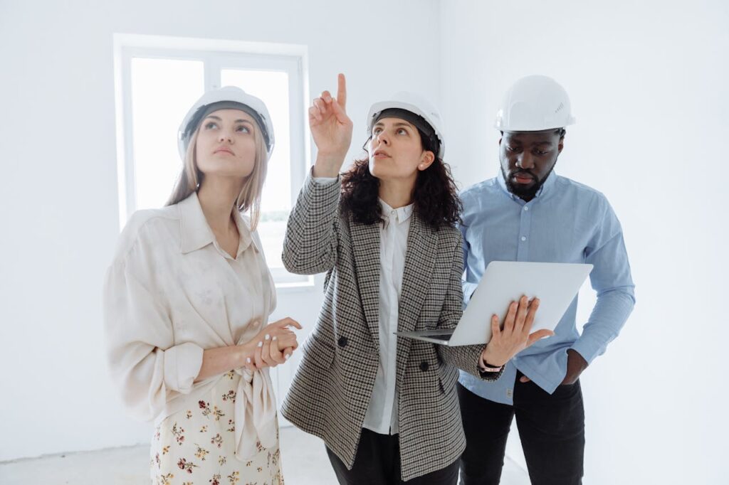Three professionals in hard hats conducting an indoor building safety inspection with a laptop