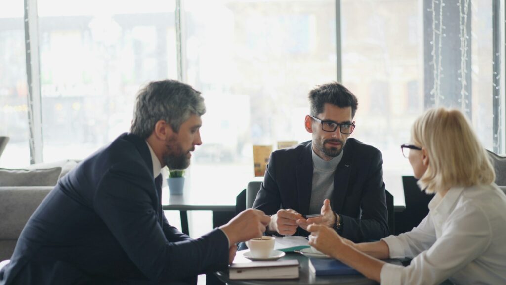 Homeowner consulting with a public adjuster about insurance documents at a café meeting