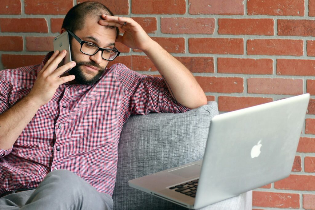 Concerned homeowner on the phone while reviewing rising insurance costs on his laptop.